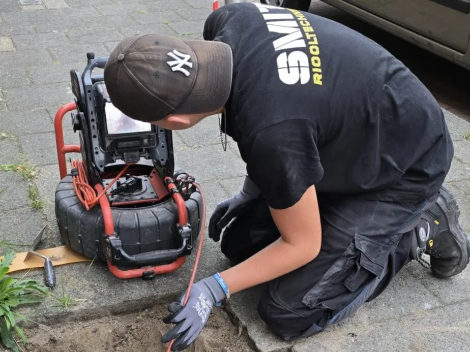 Monteur knielt op de stoep en bedient de haspel van een inspectiecamera met beeldscherm