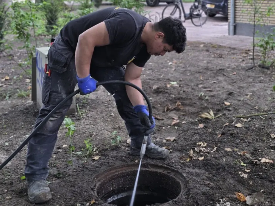 Monteur spuit een put in een plantsoen door met een hogedrukslang