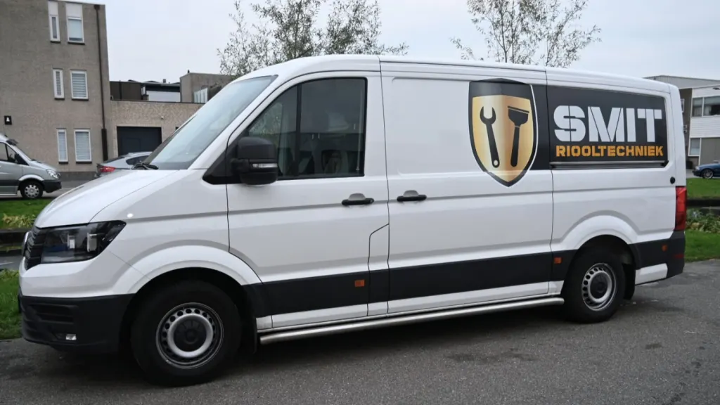 Witte bestelbus van SMIT Riooltechniek met zwarte band en gouden schild, van opzij gezien