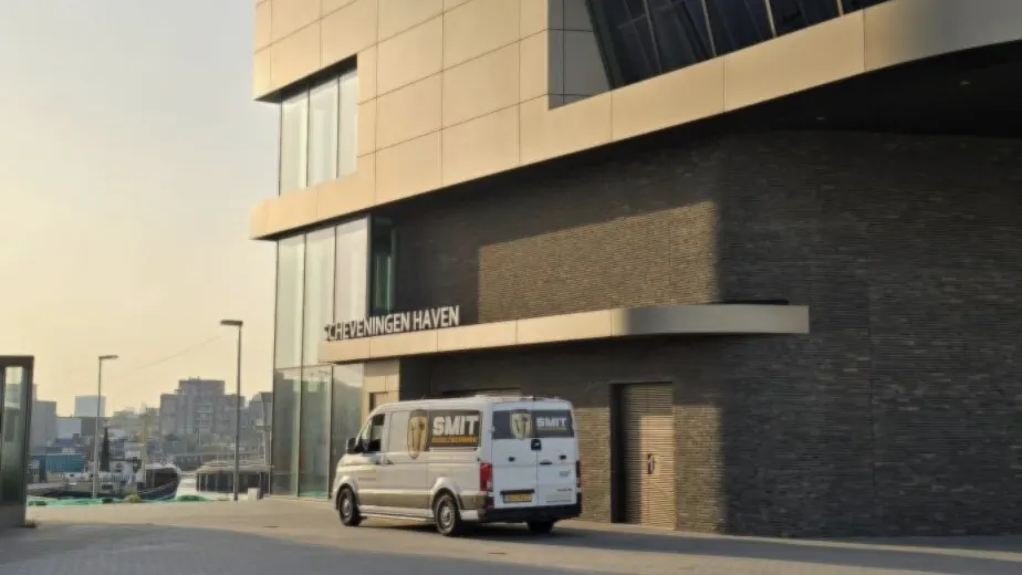Witte bus van SMIT Riooltechniek voor een modern gebouw aan het water, in het avondlicht