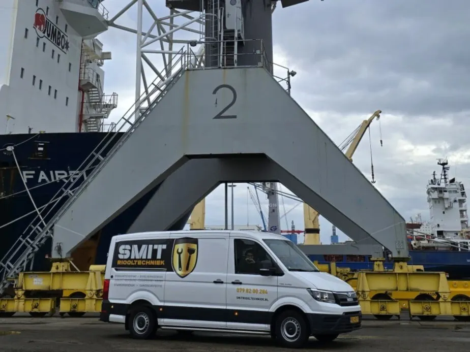 Witte bus van SMIT Riooltechniek op een havenkade, onder de poot van een grote kraan