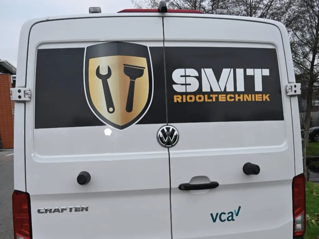 Achterkant van een witte bus met het schild en de naam SMIT Riooltechniek op de deuren