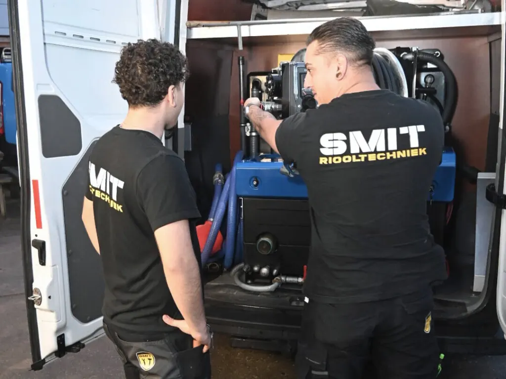 Twee monteurs bij de hogedrukunit achter in de bus; de een legt de ander iets uit