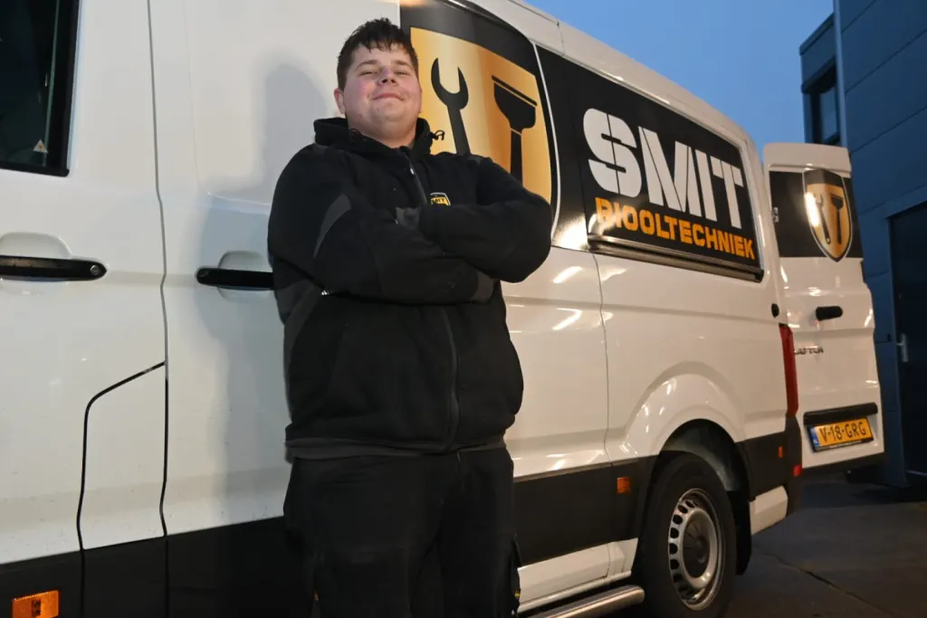 Monteur in zwarte jas met de armen over elkaar voor een bus van SMIT Riooltechniek