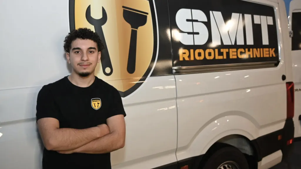 Jonge monteur met de armen over elkaar voor het schild en de naam op een bus